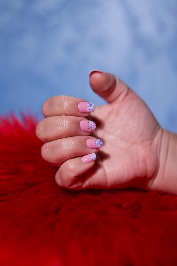 Soft pink glitter nails for nail biters showing a clean and natural short nail look