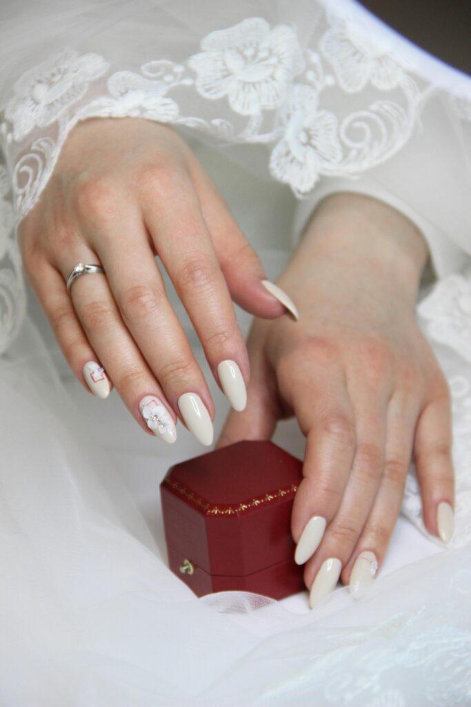 Simple cream almond wedding nails 2026 with lace bridal dress and red ring box
