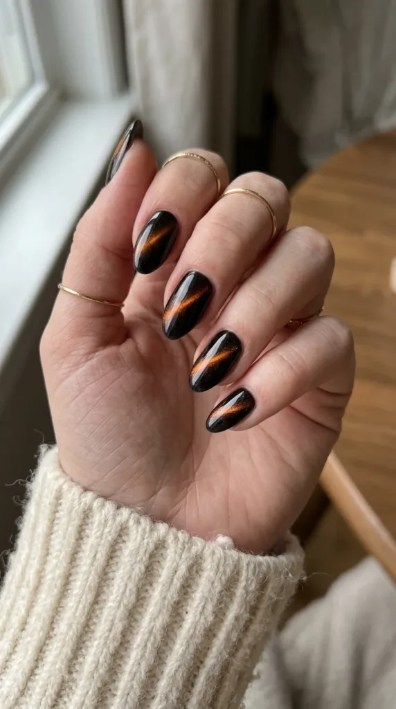 almond halloween nails: black cat eye almond nails with a glowing orange magnetic line