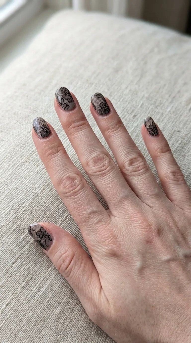 Sheer black lace pattern nails over a soft grey base on a linen cloth