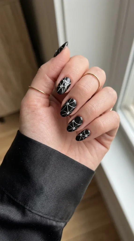 glam halloween nails: glossy black nails with a silver web and tiny clear crystals at the intersections