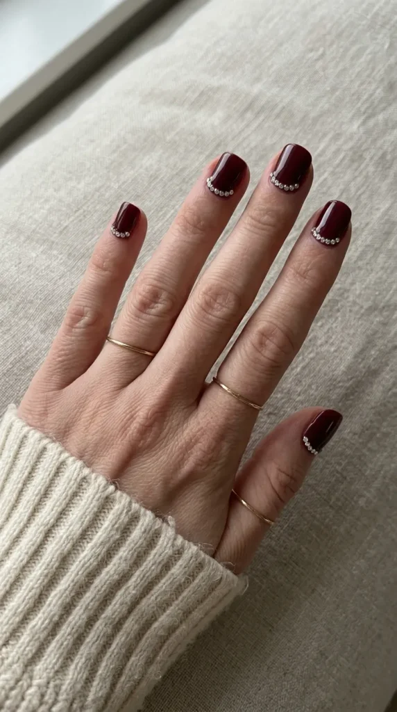 Burgundy nails with a curved row of small rhinestones along the cuticle