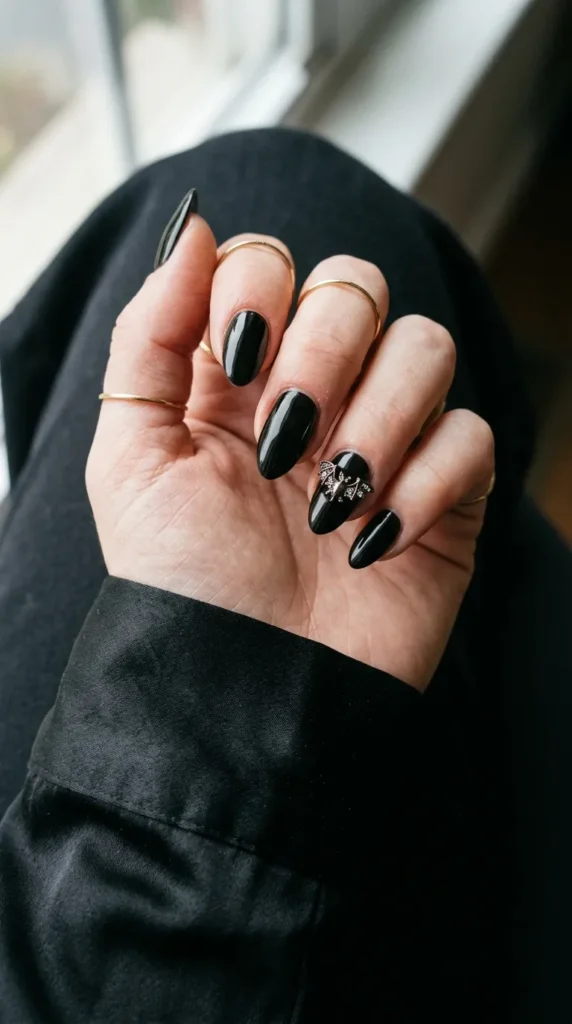 Black nails with a small metal bat charm set with tiny crystals