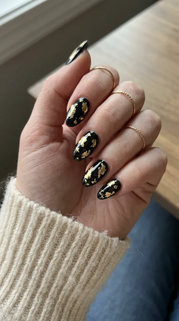 glam halloween nails: black nails with irregular patches of gold foil and a glossy finish