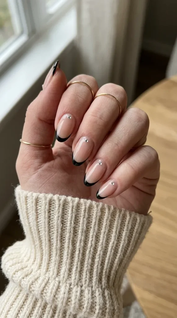 Sheer nude nails with black tips and a single small crystal at the smile line