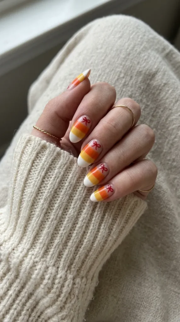 Candy corn striped nails in white orange and yellow with a small red bow