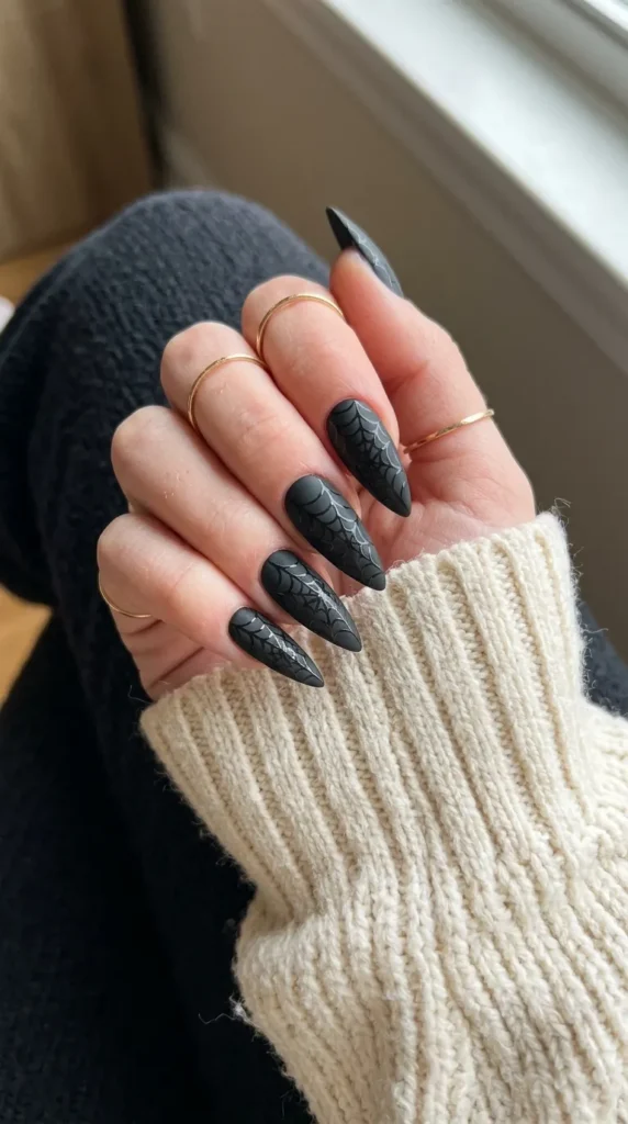 Matte black stiletto nails with a subtle glossy spiderweb