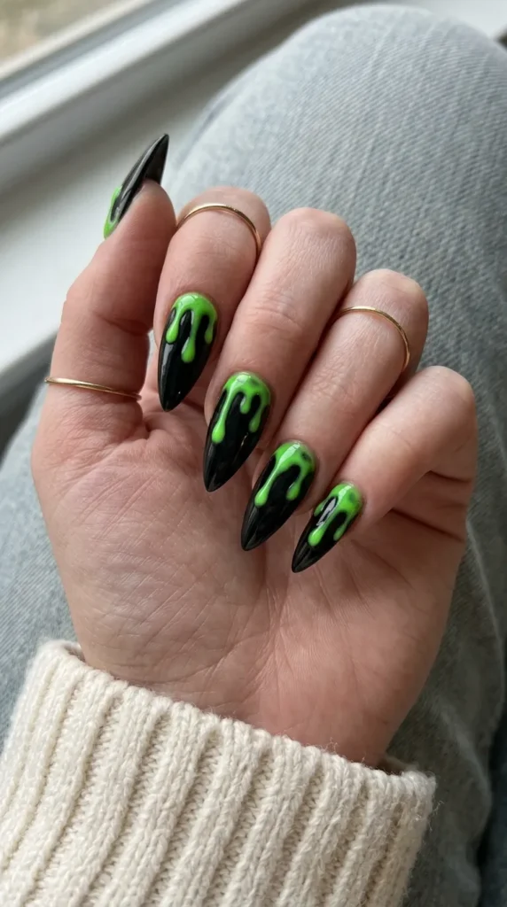 stiletto halloween nails: black stiletto nails with neon green slime drips from the cuticle