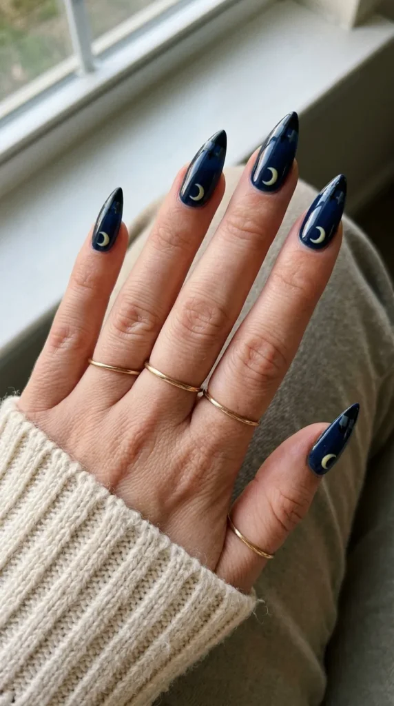 Dark blue stiletto nail with a yellow moon and black headstones at the tip
